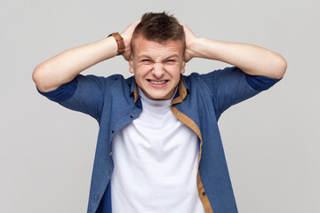 Portrait of sad upset handsome teenager boy wearing blue shirt standing with hands on head,...