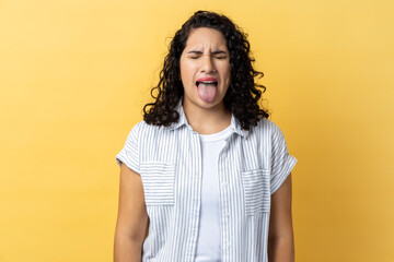 Portrait of woman with dark wavy hair sticking out tongue and looking at camera, teasing with...