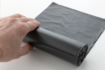 hand unwinds a roll of plastic garbage bags, a black polyethylene waste container on a white...