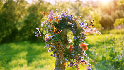 flowers wreath on wooden post and butterflies on sunny meadow natural background. Floral crown,...