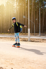 happy child schoolboy with a backpack goes to school on a skateboard. a joyful boy with protection...