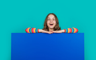 happy shocked child behind blank blue paper with copy space for advertisement