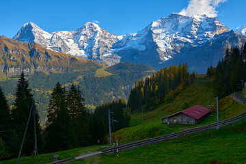 Fototapeta na wymiar Mountain view of Jungfrau, Monch, Eiger peaks at sunset with old barn and railroad in Switzerland Bernese region.