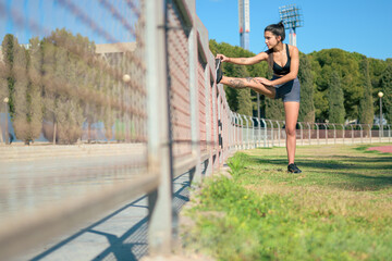Female athlete with tattoos performs stretching in a park in a sunny day