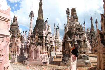 Turista con gorro y falda haciendo una foto a una estupa de Kakku, en Myanmar, Birmania, entre...