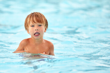 Little boy in the pool with a displeased face, surprised kid in the water of the pool, copy space.