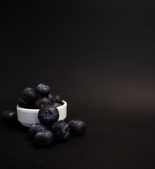 Blueberry berries in a white bowl on a black background