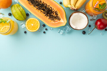 Exotic paradise concept. Top view of tropical fruit juice or cocktail in a glass jar, kiwi, papaya, orange, carambola and coconut on a blue background with an empty space for advertisement