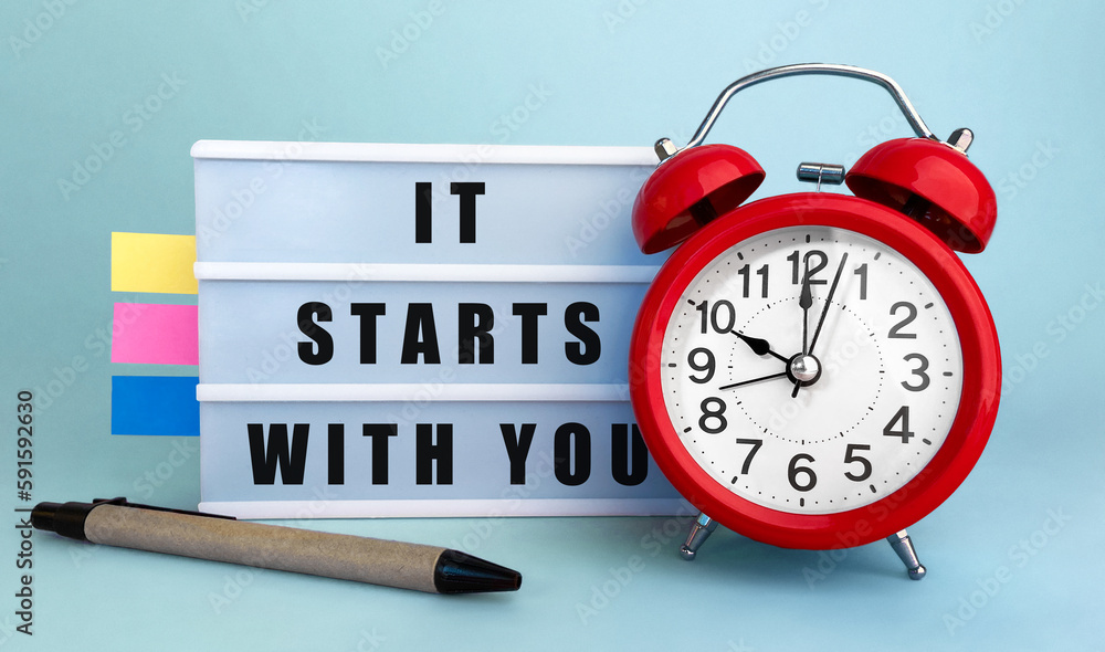 Poster text it starts with you written on the lightbox with alarm clock and colorfull stickers on blue back