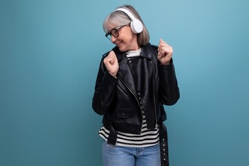 energetic stylish modern elderly woman with gray hair listens to music in headphones on a bright background with copy space