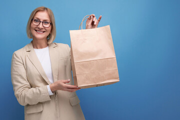 middle-aged business concept. smiling woman in jacket holding package on studio background with copy space