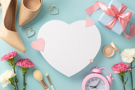 Top view flat lay photo featuring high-heels, earrings, makeup brushes, a gift box, and lovely carnation flowers on a pastel blue background with empty heart for advert