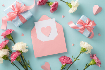 Mother's Day sentiment concept. Top view flat lay photo of postcard, gift boxes with pink ribbons, carnation flowers, and pink paper hearts on pastel blue background