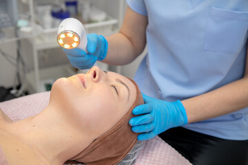 Calm and relaxed female patient sleeping and getting modern rejuvenation laser facial procedures in spa clinic salon