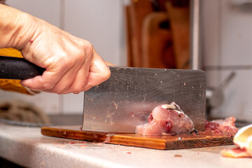 A woman cuts fish with a large knife at home in the kitchen