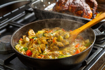 Frying pan with stewed vegetables in sauce and spices and a wooden spoon on the stove .