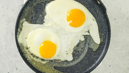 Fried eggs on a hot frying pan, view from above, copy space Traditional breakfast recipe