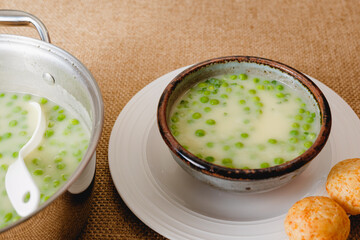 Celery cream soup with a green pea served with freshly baked cheese bread close-up on rustic background
