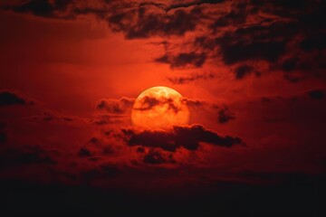 red sun with clouds behind on the dark sky, a red sun with clouds in the background