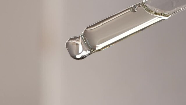 Cosmetic dropper close-up. Dripping essential oil from a pipette on a beige background.