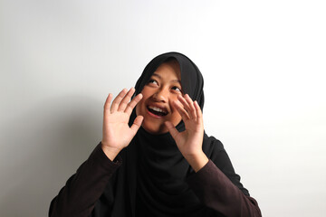 Cheerful young Asian girl in hijab shouting loudly telling about good news isolated on white background.