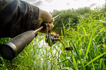 Obraz premium Male hand holding spinning rod on the background of the river.