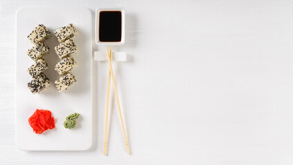 Sushi roll California with salmon, sesame seeds, avocado, cream cheese on white background. Rolls served on white dish with wasabi, ginger and soy sauce. Japanese cuisine food. Top view, copy space