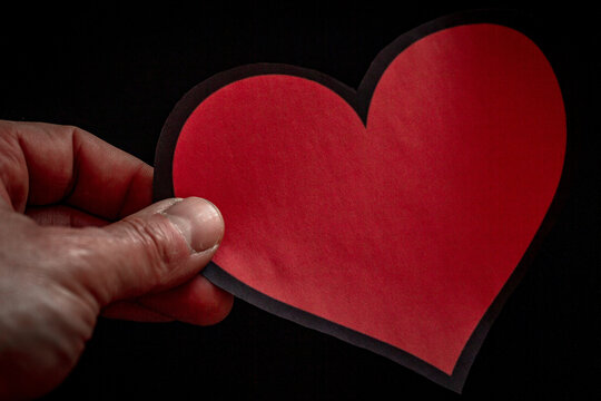 mano che regge un cuore rosso su sfondo nero