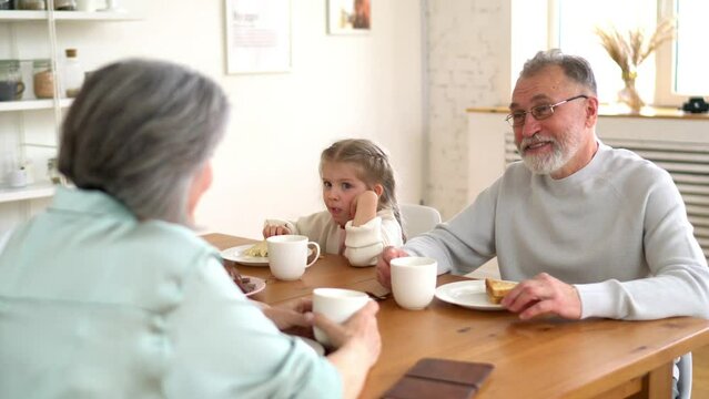 Caucasian couple in love spending time with cute grandchild talking about family relationship during breakfast time in dining room, granny people during morning routine with child
