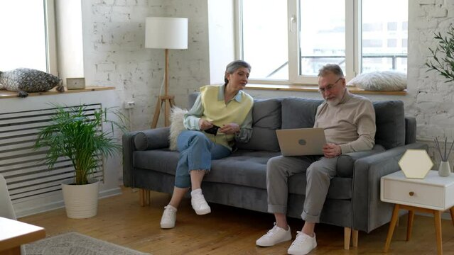 Caucasian couple in love spending weekend time togetherness with playful granddaughter resting in home living room, happy wife kitting while skilled hasband using laptop for working remotely
