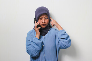 Thoughtful young Asian girl in hijab looks confused while on a phone call