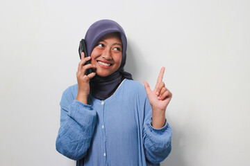 Young Asian girl in hijab makes a phone call while pointing fingers aside
