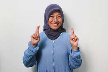Young Asian girl in hijab holding fingers crossed