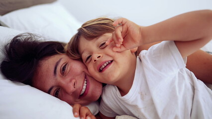 Lifestyle moment of mother and child lying in bed looking at camera smiling. Motherhood happiness concept