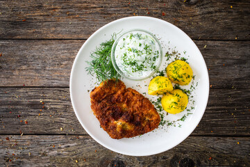 Top view of breaded fried pork chop with fresh cucumber in cream and potatoes on wooden table
