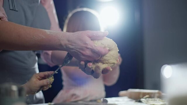 The daughter helps her mother roll out the dough for baking. The family cooks together in the kitchen. High quality 4k footage
