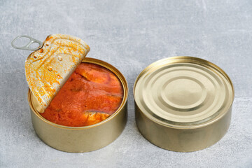 Open tin can with fish in tomato on gray concrete background.