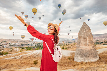 Standing in a scenic valley in Cappadocia, the girl in an exquisite dress admires the sky dotted...