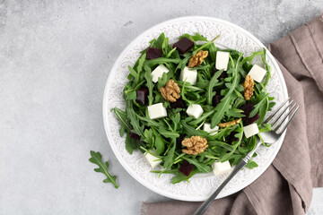 Beetroot salad with feta cheese, arugula and walnuts on a gray background. Top view. Copy space.