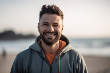 Portrait of smiling man in hoodie standing on beach at sunset