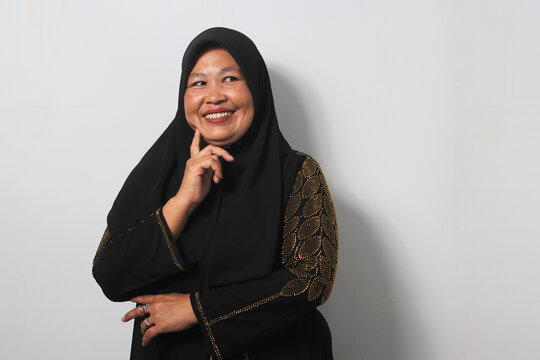 Pensive Middle aged Asian women wearing hijab touches hand chin while look away on copy space
