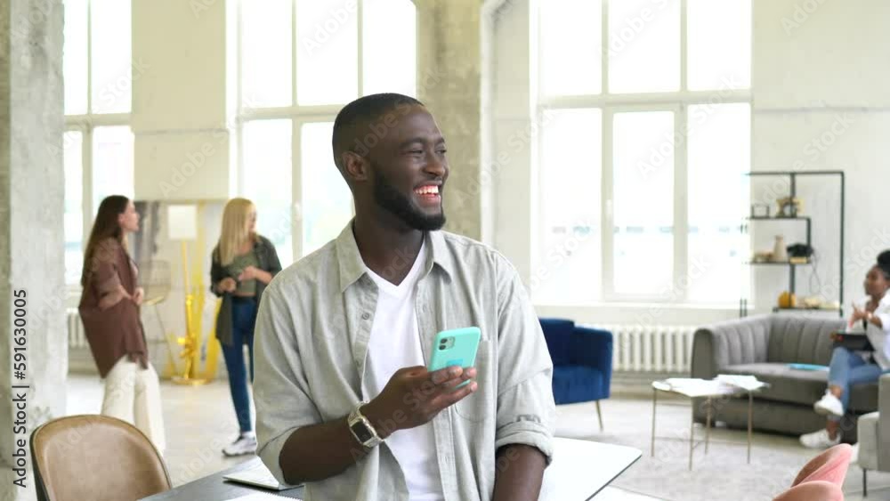 Poster happy dark skinned male blogger using cellphone device for messaging and chatting with network frien