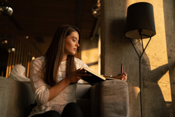 Portrait of a young smiling charming woman putting notes in agenda