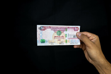 Man hand holding 100 Dirhams, united arab emirates currency on black background