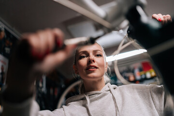 Closeup low-angle view of pretty blonde cycling mechanic female repairing and fixing mountain...
