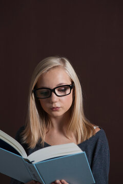Portrait of Blond, Teenage Girl wearing Eyeglasses and Reading Book, Studio Shot on Black Background