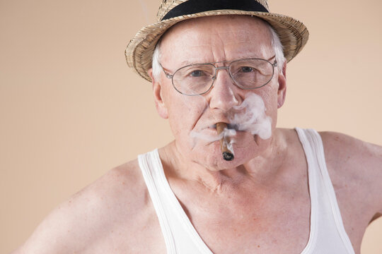 Portrait of Senior Man wearing Undershirt and Straw Hat while Smoking Cigar, Studio Shot on Beige Background