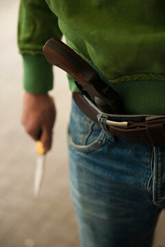 Close-up of Young Man holding Knife with Handgun tucked into Waistband of Blue Jeans, Mannheim. Baden-Wurttemberg, Germany