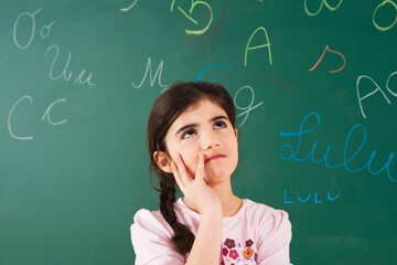 Girl Looking up and Thinking in front of Chalkboard in Classroom