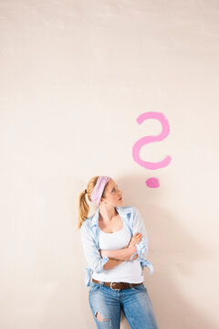 Studio Shot of Young Woman Leaning Against Wall with Question Mark